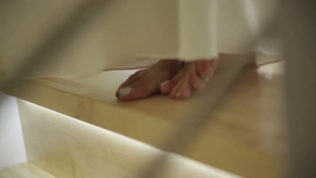 Woman In A White Dress Walks Down The Stairs. Close-up Of Feet.
