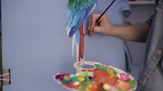 Girl With A Brush Paints A Parrot On The Canvas.