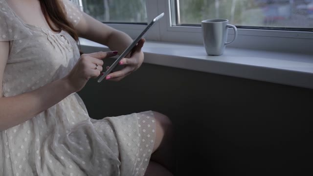 Girl With Tablet Sitting By The Window. Close-up.