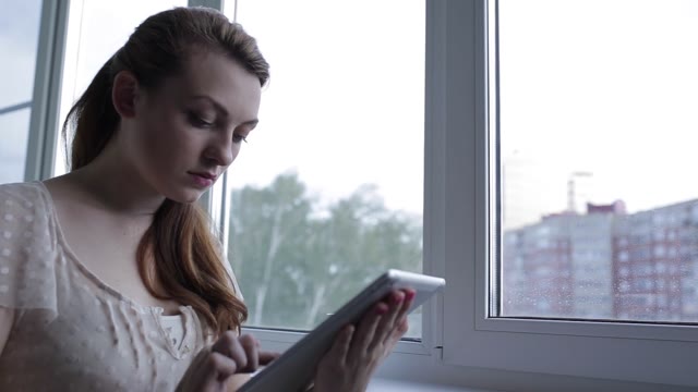 Girl Sitting By The Window And Using Digital Tablet. Close-up.