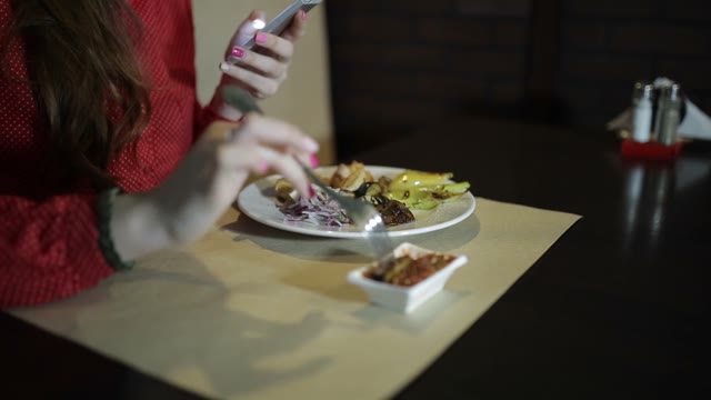 Beautiful Girl In Red Dress Eating In A Restaurant And Holding A Smartphone.