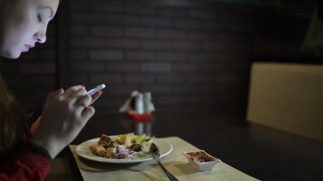 The Girl In The Red Dress Sits At A Table In The Restaurant And Use The Phone