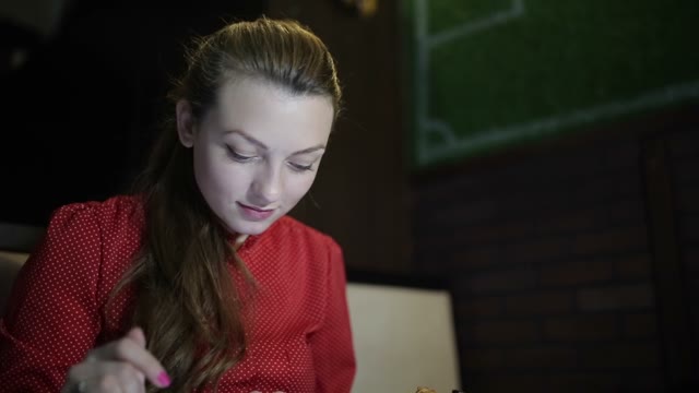 A Woman In A Red Dress Is Using A Tablet At The Table Of The Restaurant.