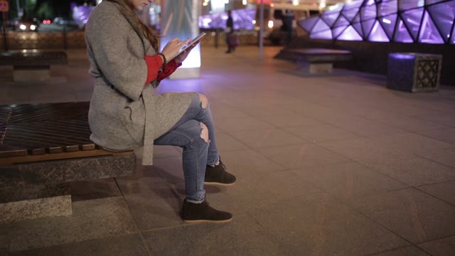 Cute Woman In A Coat Using A Tablet On The Street At Evening.