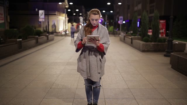 A Young Girl Stands On The Boulevard With A Tablet In The Evening.