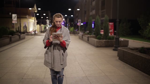 Young Girl In A Coat Is On The Boulevard And Enjoys The Tablet.