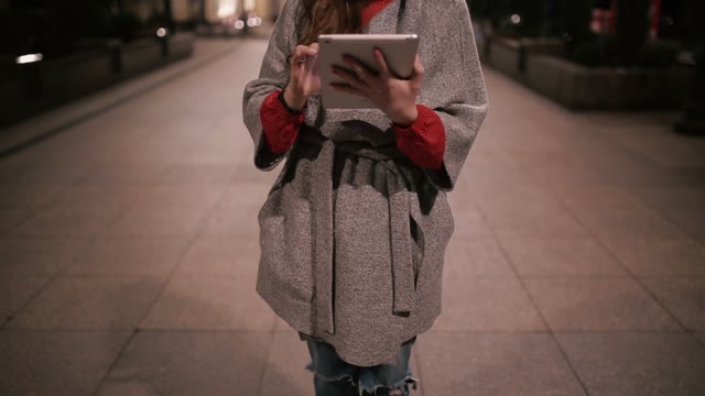 Young Girl Working In A Coat With A Tablet On The Street At Night.