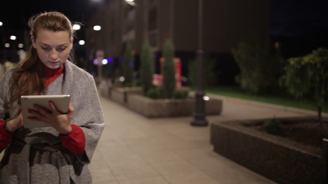 Beautiful Girl In A Coat Is On The Boulevard And Uses Tablet.
