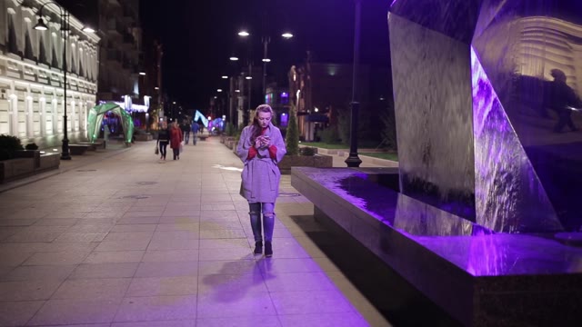 Young Girl Walking Down The Street And Looking At The Phone.