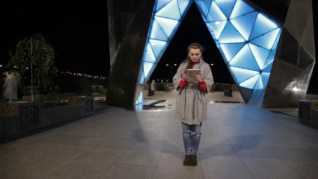 Girl Stands And Using A Tablet In The Evening. Shining Arches Fountain.
