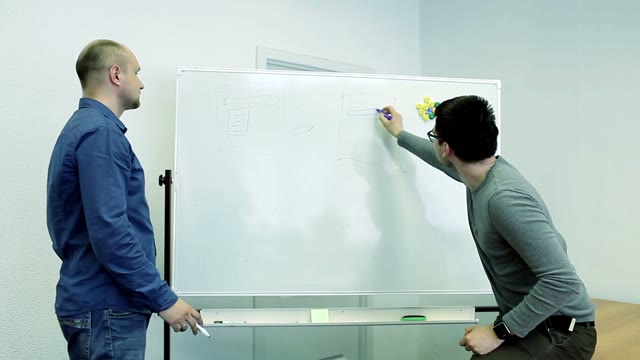 Two Men Draw Diagrams On A White Board And Discussing Something