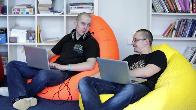 Two Young Man With A Laptop Sitting On A Chair And Talking