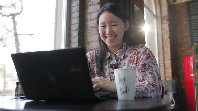 Woman Sitting In A Cafe With A Laptop And Coffee And Smiling