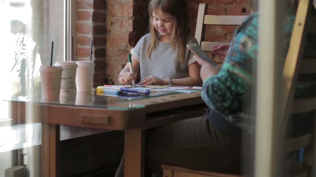 Child At The Table Draws On A Paper And Smiles