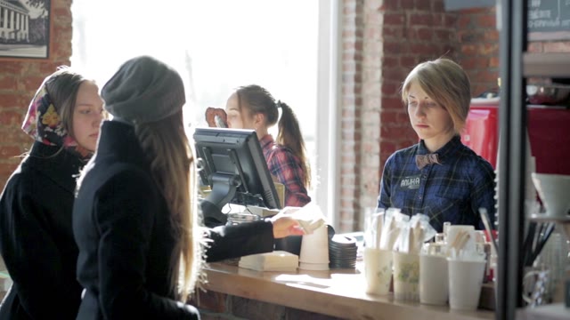 A Young Girl Cashier In A Cafe Takes Money From Visitors