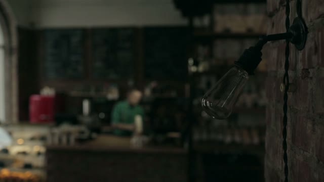 Close Up Of A Lamp Lights In A Cafe. The Staff Behind The Bar In The Background