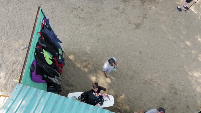 Young People On The Beach Taking Of Sports Equipment Storeroom. View From Top.