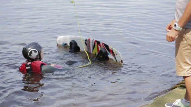 Beautiful Young Girl Begins To Ride A Wakeboard Under The Supervision