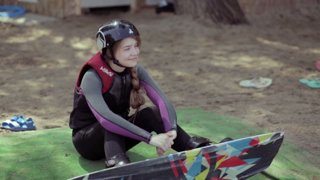 The Girl With Wakeboard On His Feet Sits And Looking Into The Distance.