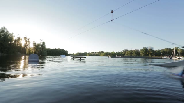The Young Man Fast Rides On A Wakeboard Against The Sunset In The Wake Park