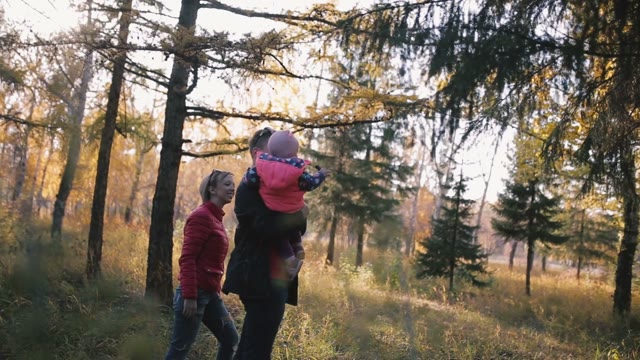 Happy Family With A Child In Her Arms Walks In The Woods. Shines Autumn Sun