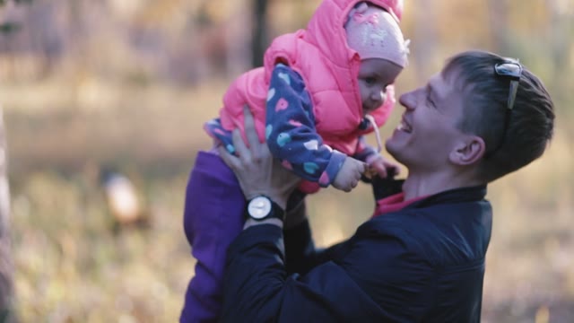 Father Holding His Child And Kisses On The Cheek. Autumn In The Park.
