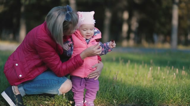 Mother And Little Daughter On The Field Picking Flowers.