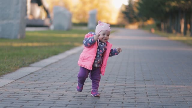 In Autumn Park Little Girl Making First Steps, Her Mother Helps Her.