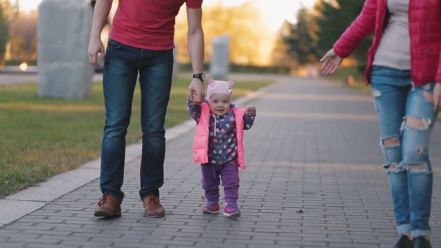 Happy Child Is Learning To Walk With His Father And Mother.