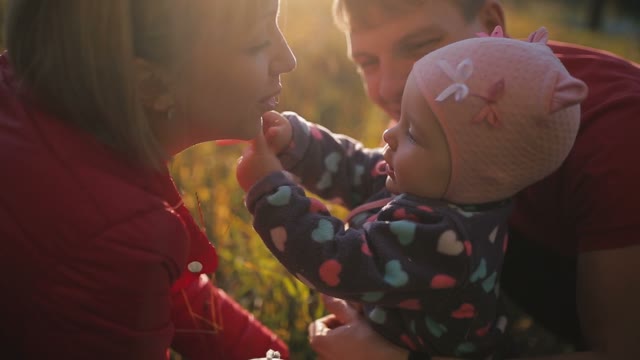 Happy Family Sitting In The Autumn Field. The Girl Pulls Hands To Face Mother.