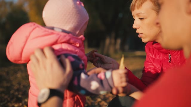 Happy Parents Give A Child Fallen Leaves In The Autumn Field.