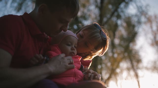 Happy Family Holding A Child In Her Arms. Behind The Trees.