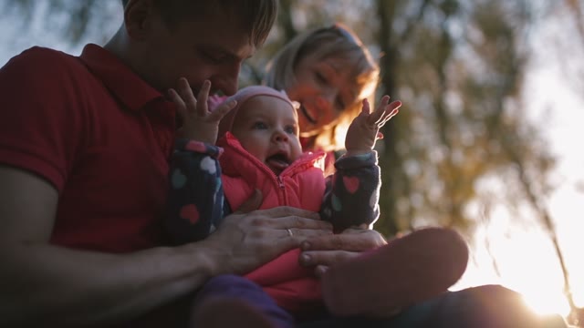 Happy Family Holding A Baby In Her Arms. The Sun Is Shining.