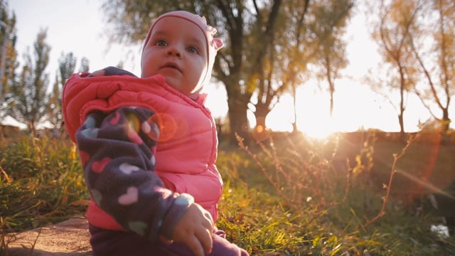 Little Girl Sitting At The Autumn Meadow, The Sun Shines On It. Autumn Sunset.