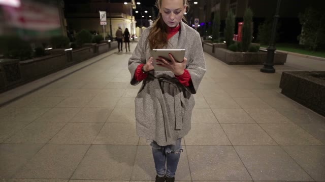 A Young Girl Stands On The Street With A Tablet In The Autumn Evening .
