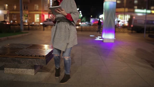 The Girl Sits On A Bench In The Street And Works With The Tablet.