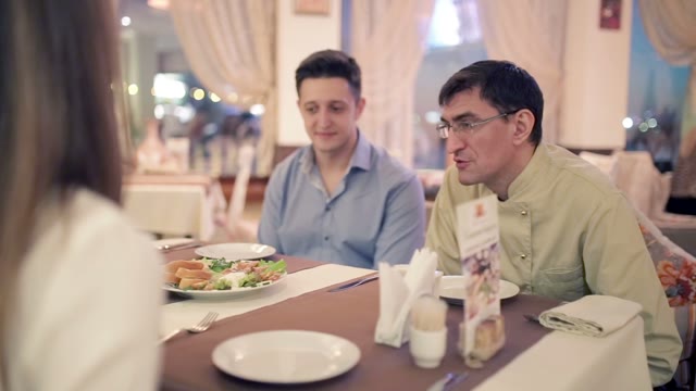Two Men With Girl Sitting At A Table In A Restaurant.