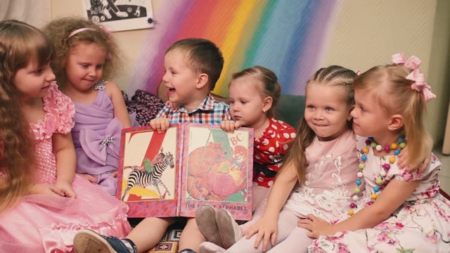 The Boy Is Holding A Book, And The Girls Laugh.