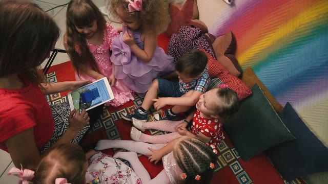 A Young Girl Shows Children Playing On A Tablet.