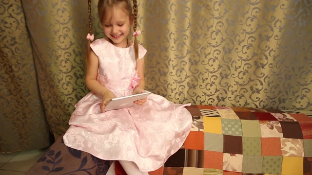 Lovely Girl In A Pink Dress Sitting And Playing With The Tablet.