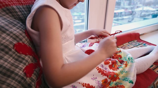 Little Girl Sitting By The Window And Pulls The Red Yarn On A Stick.