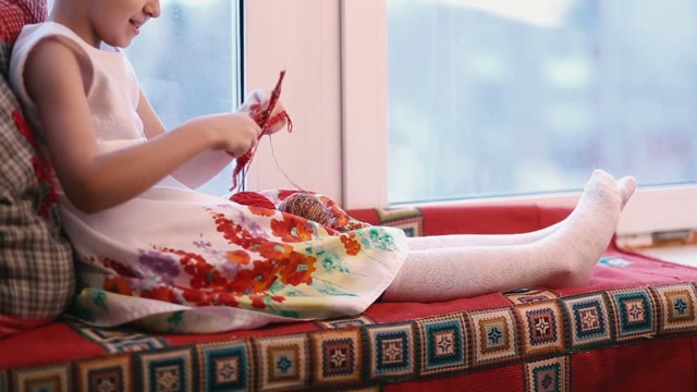 Little Girl In White Sitting At The Window And Making Crafts.