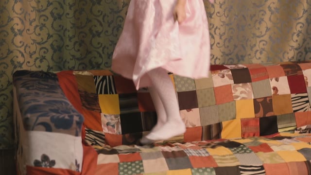 Little Girl Jumping On The Couch And Looking At The Camera.