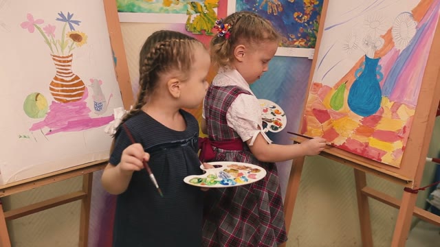 Two Little Girls Standing At The Easel And Paint.