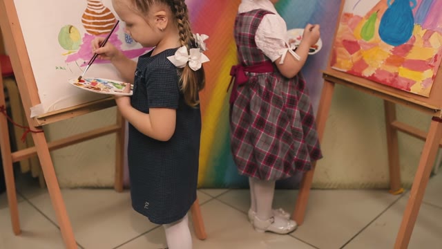 Two Little Girls Standing At The Easel And Paint.