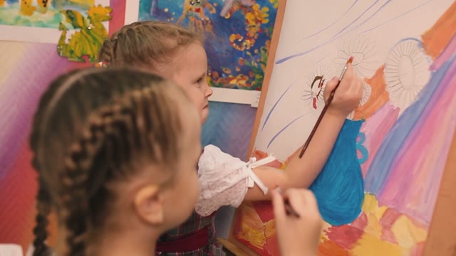 Two Little Girls Standing At The Easel And Paint.