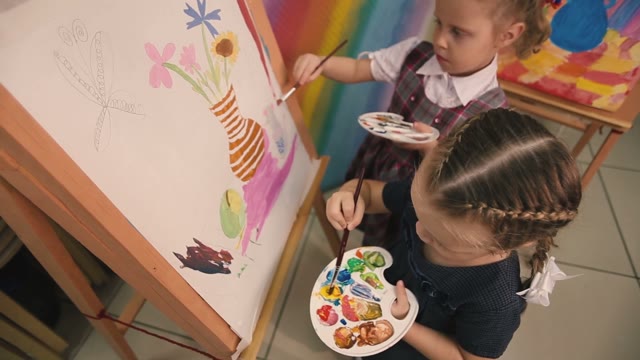 Two Little Girls Sit And Paint Brushes On Canvas. Top View.