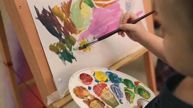 Girl Draws On The Easel With A Brush .