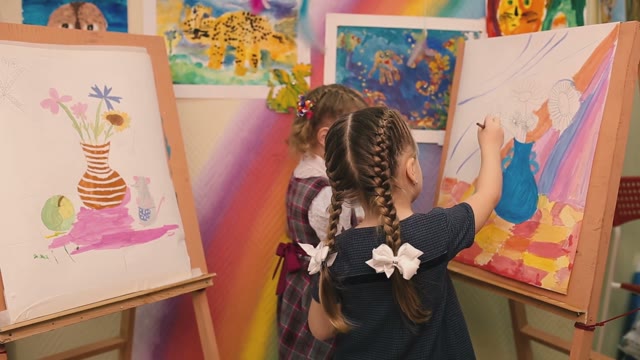 Two Little Girls Sit And Paint Brushes On Canvas.