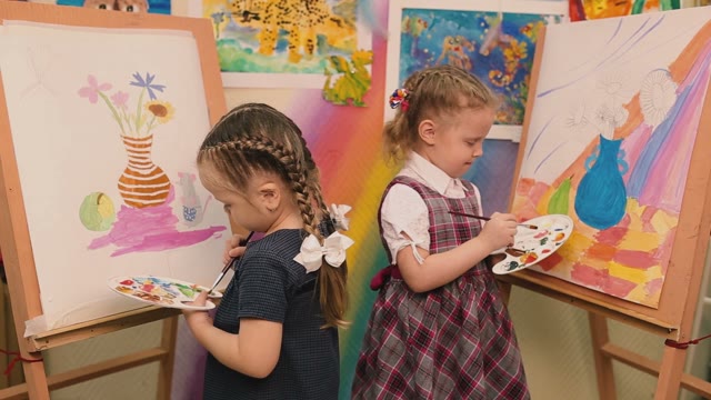 Two Little Girls Standing At The Easel And Paint Colors.